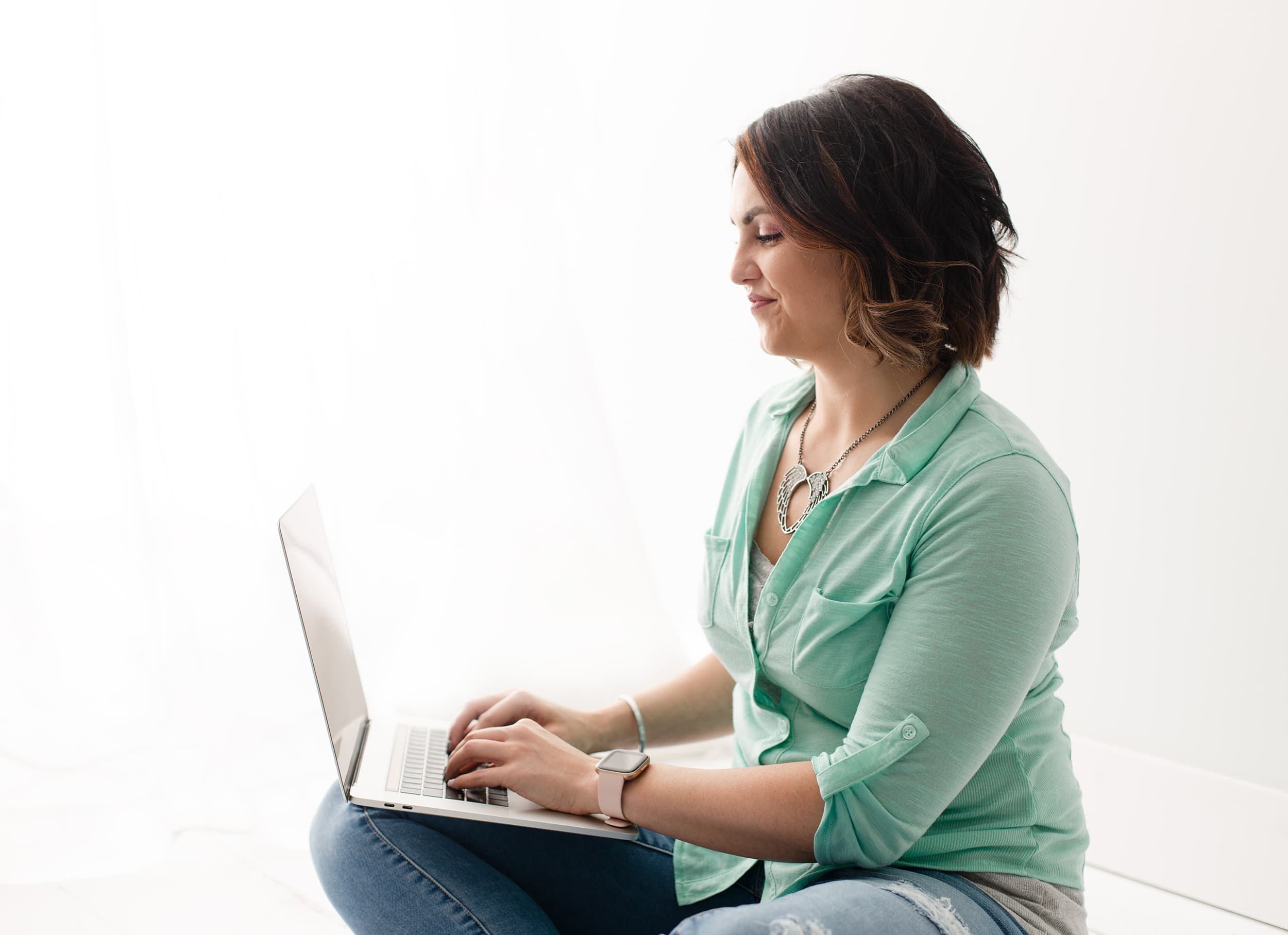 Megan sitting cross-legged on the floor smiling at the open laptop in her lap, taken from the side