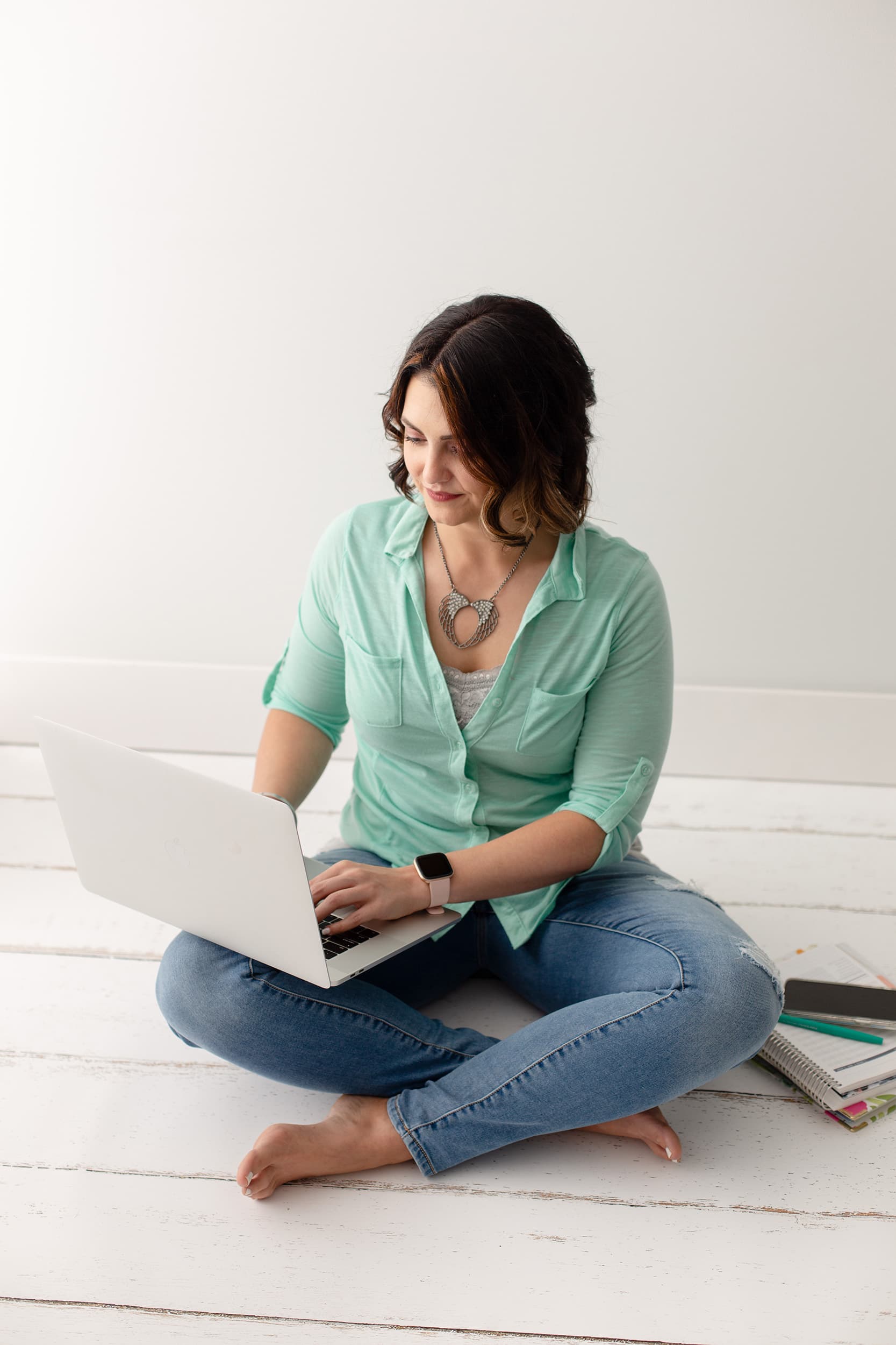 Megan sitting cross-legged in the floor, looking down at the laptop balanced on one knee